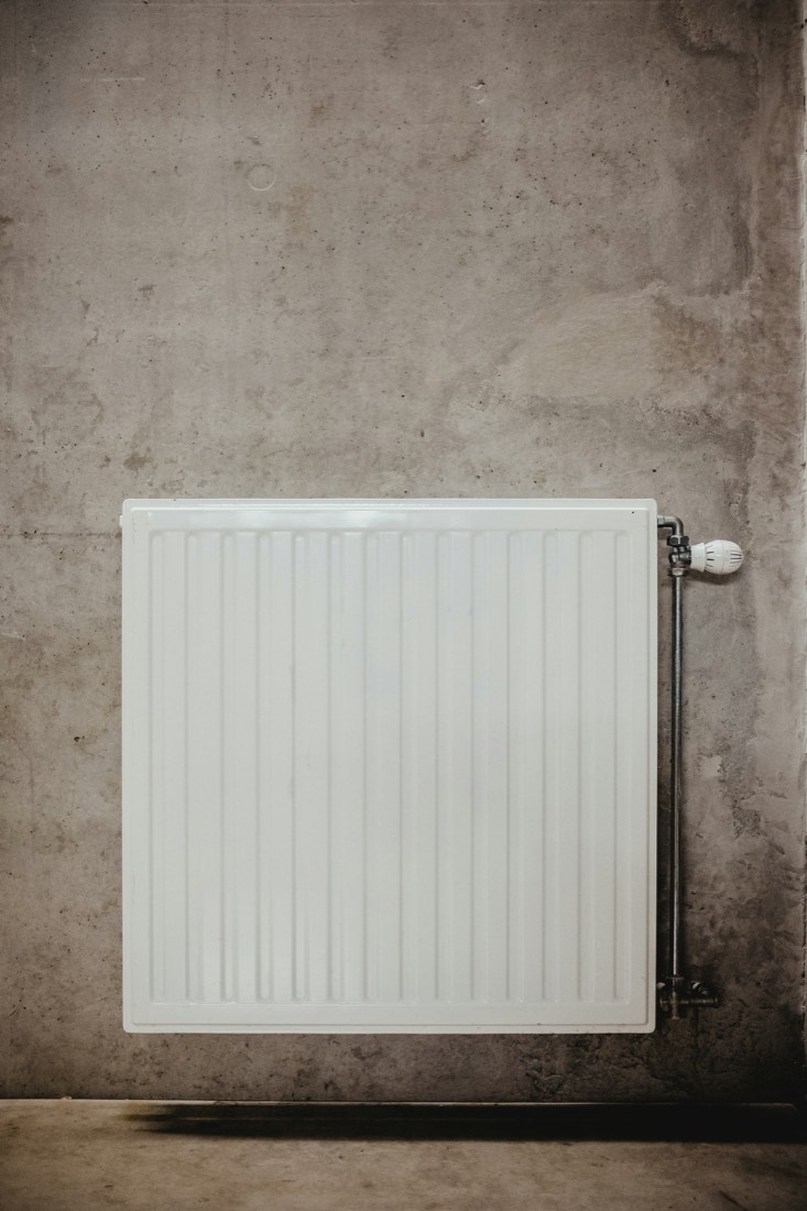 Radiateur à eau blanc avec robinet thermostatique sur mur brut